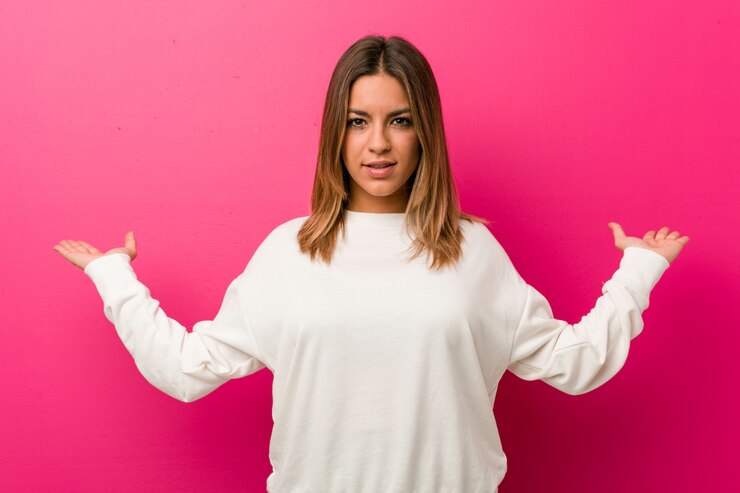 Foto joven auténtica mujer carismática de personas reales contra una pared hace escala con los brazos, se siente feliz y confiada.