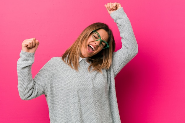 Joven y auténtica mujer carismática de personas reales contra una pared que celebra un día especial, salta y levanta los brazos con energía.