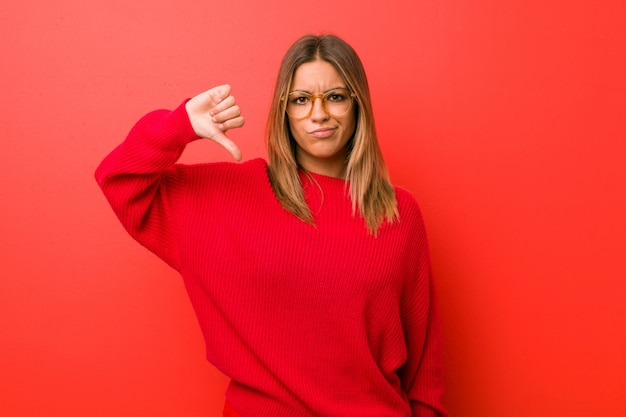 Joven auténtica mujer carismática de personas reales contra una pared que muestra un gesto de disgusto, con los pulgares hacia abajo. Concepto de desacuerdo