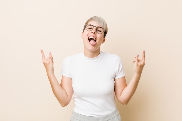 Joven auténtica mujer natural con una camisa blanca que muestra gesto de rock con los dedos