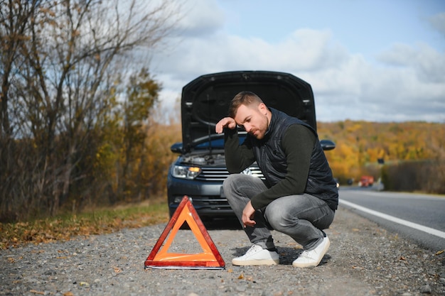 Un joven con un auto negro que se descompuso en el espacio de la copia de la carretera.