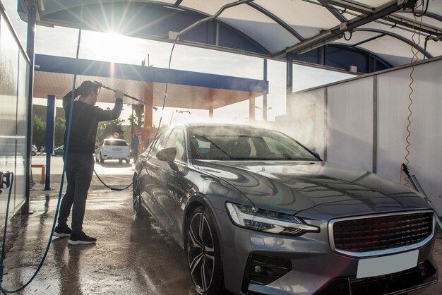 Foto joven autolavado de autos al aire libre con agua a presión manual