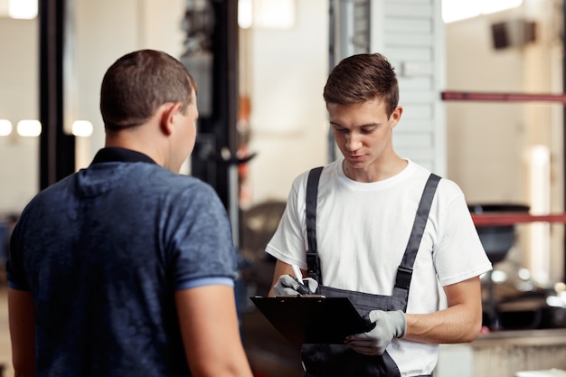 Un joven automecánico está cumplimentando un formulario sobre los resultados del trabajo realizado.