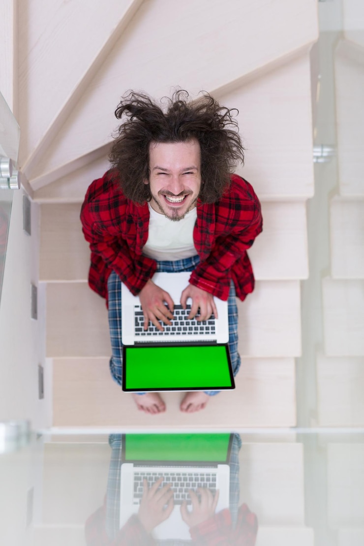 Foto joven autónomo en albornoz trabajando desde casa usando una computadora portátil mientras está sentado en las escaleras