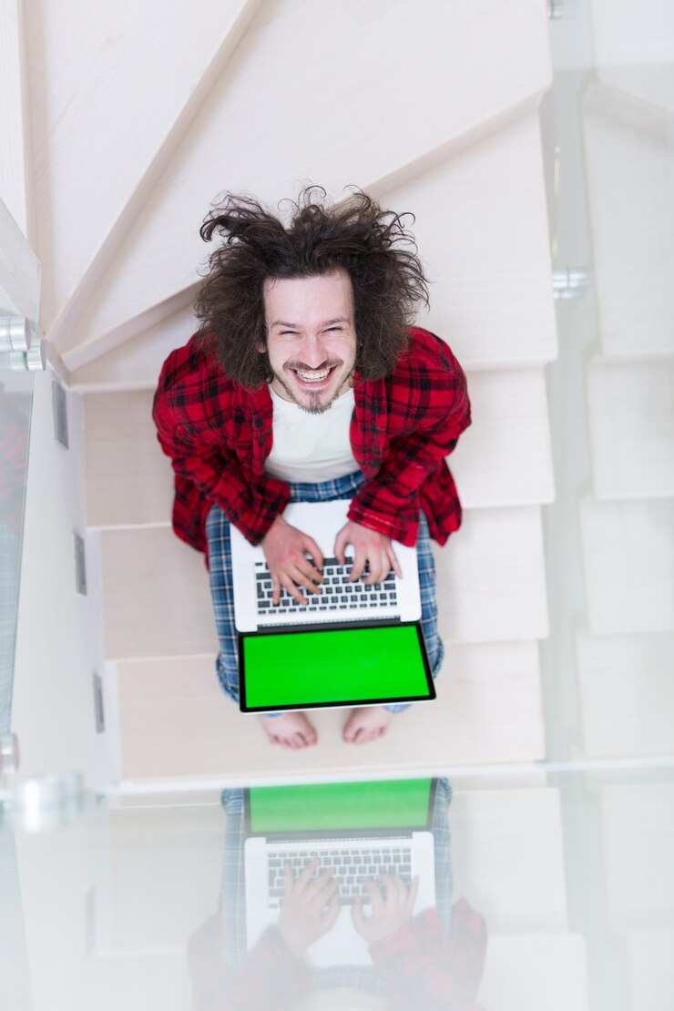 Foto joven autónomo en albornoz trabajando desde casa usando una computadora portátil mientras está sentado en las escaleras