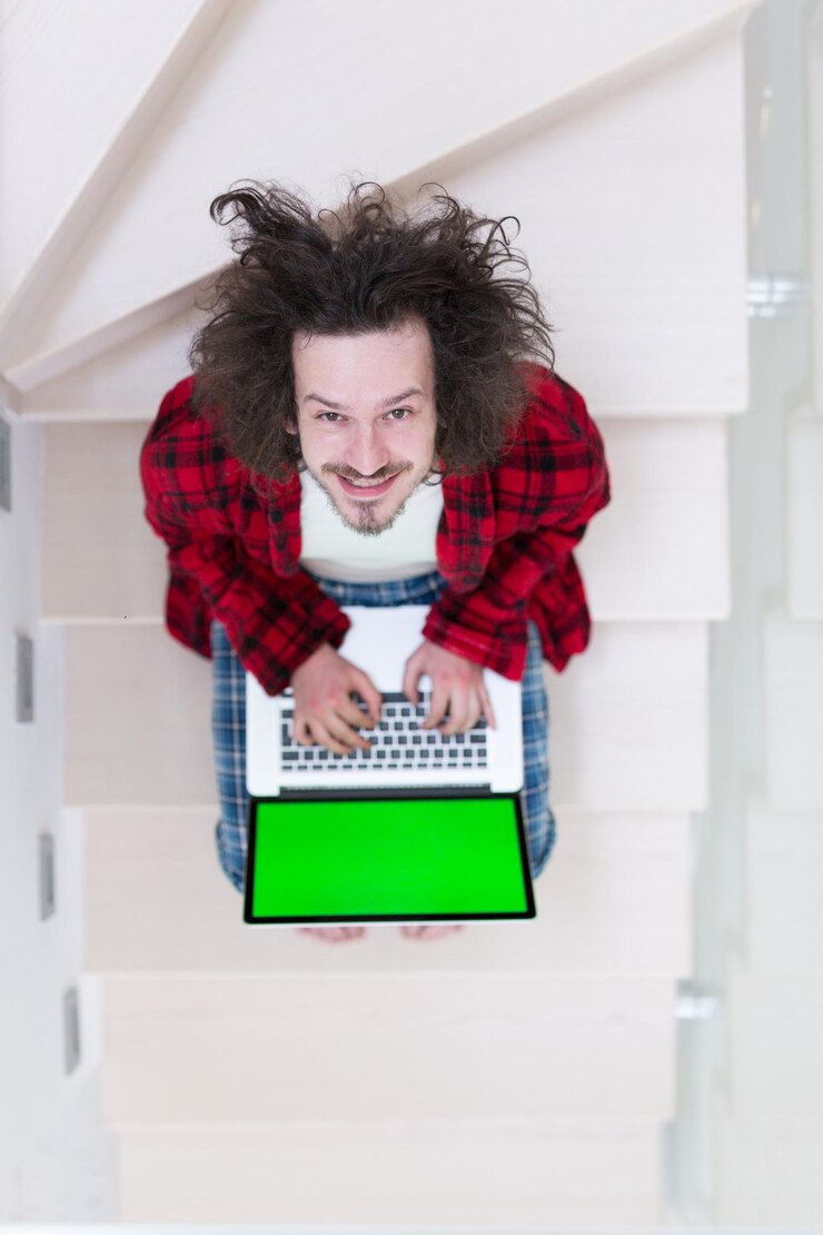 Foto joven autónomo en albornoz trabajando desde casa usando una computadora portátil mientras está sentado en las escaleras