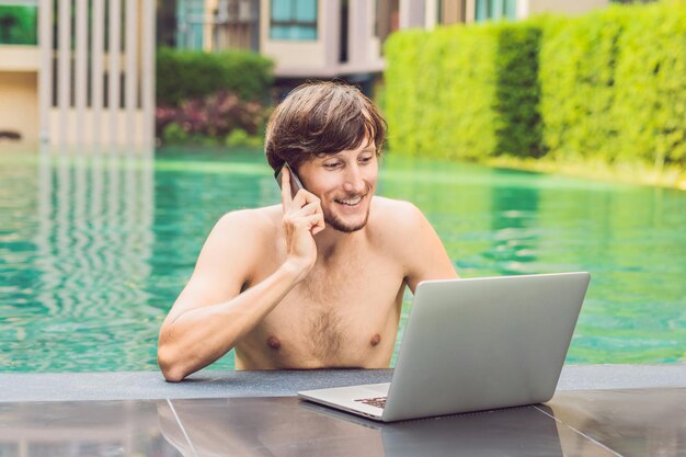 Joven autónomo que trabaja de vacaciones junto a la piscina.