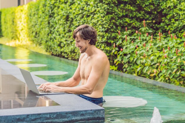 Joven autónomo que trabaja de vacaciones junto a la piscina.