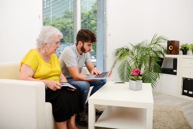 Joven ayudando a una anciana a hacer trámites y trámites administrativos con una computadora portátil en casa