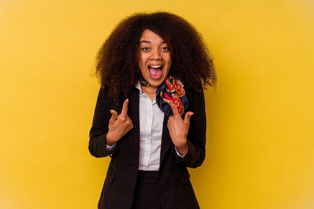 Joven azafata afroamericana aislada sobre fondo amarillo sorprendido señalando con el dedo, sonriendo ampliamente.