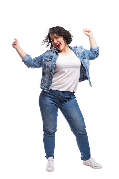 Joven bailando regordeta. Hermosa morena rizada con labios rojos en jeans. Positividad corporal y libertad. Aislado sobre fondo blanco. Vertical.