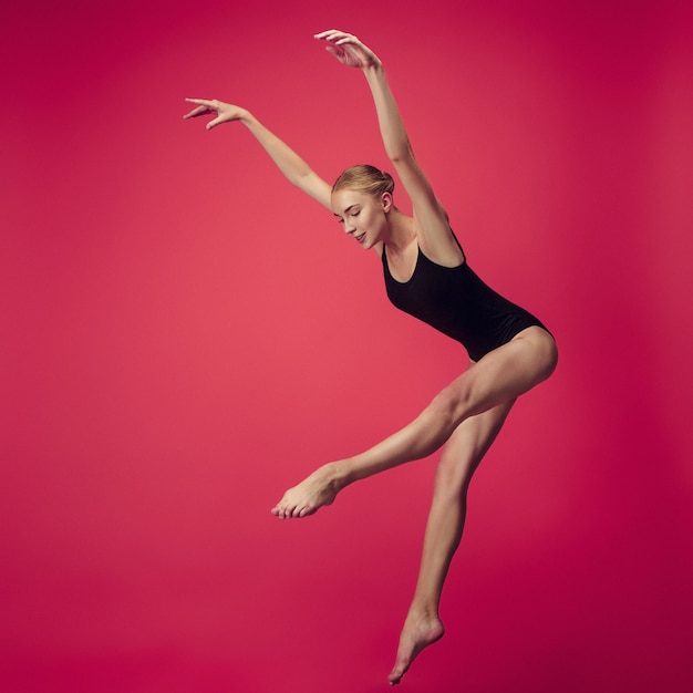 Joven bailarina adolescente bailando sobre fondo rojo de estudio. Proyecto de bailarina con modelo caucásico. El ballet, danza, arte, contemporáneo, concepto de coreografía.