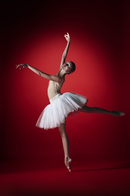 Joven bailarina de ballet femenino agraciado o bailarina clásica bailando en el estudio rojo. Modelo caucásico en zapatillas de punta