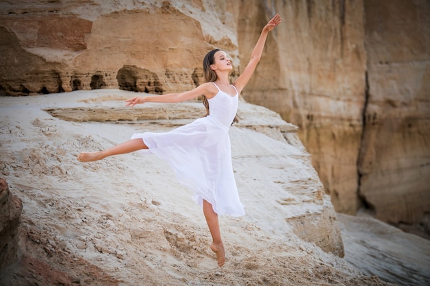 Joven bailarina se encuentra en una elegante pose en el borde de un acantilado arenoso