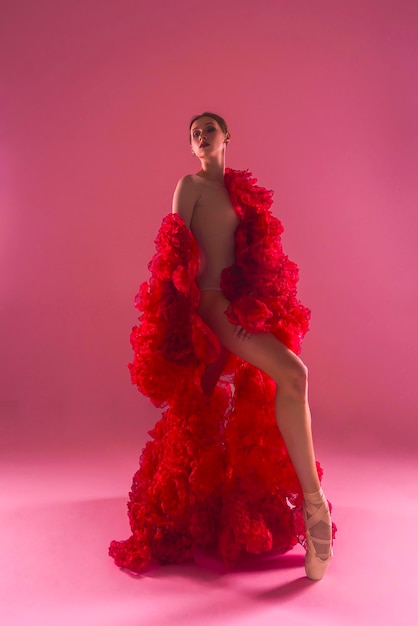 una joven bailarina en un estudio fotográfico en un vestido de capa hecho de flores de rosa muestra movimientos de ballet