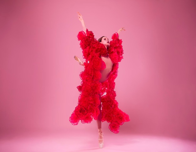 una joven bailarina en un estudio fotográfico en un vestido de capa hecho de flores de rosa muestra movimientos de ballet