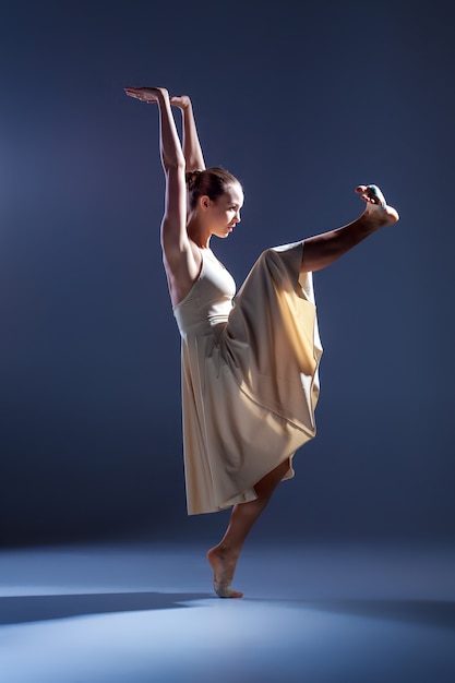 Joven bailarina hermosa en vestido beige bailando sobre fondo gris de estudio