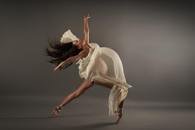 Joven bailarina hispana embarazada interpretando una pose de ballet clásico con un paño de seda en el estudio