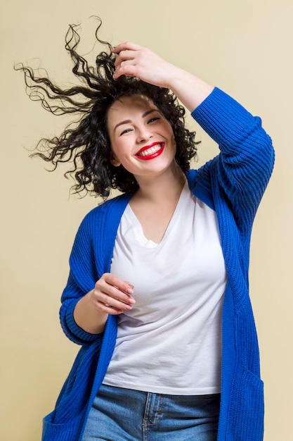 La joven bailarina se ríe Hermosa morena rizada en jeans y un suéter azul Fondo amarillo positivo y emocional Vertical