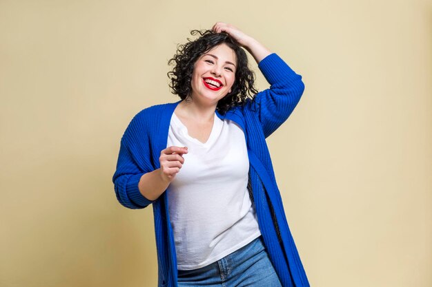 La joven bailarina se ríe Hermosa morena rizada en jeans y un suéter azul Fondo amarillo positivo y emocional