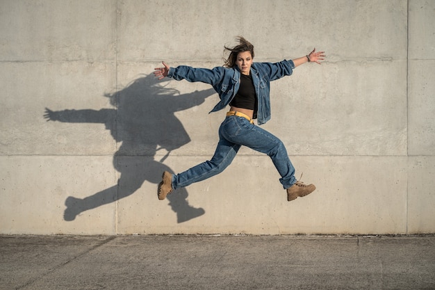 Joven bailarina saltando con un fondo gris y una sombra reflejada. Fotografía horizontal