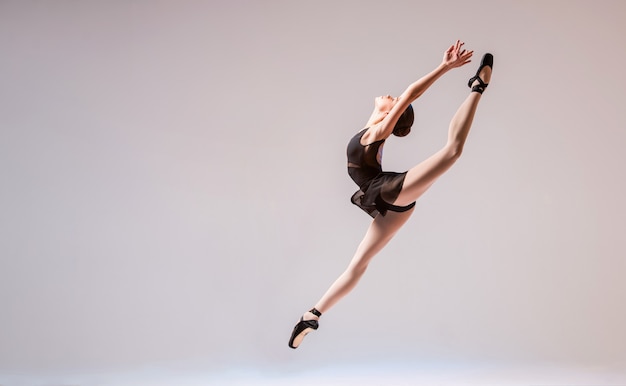 Una joven bailarina en traje de baño negro y pointes salta sobre un fondo brillante.