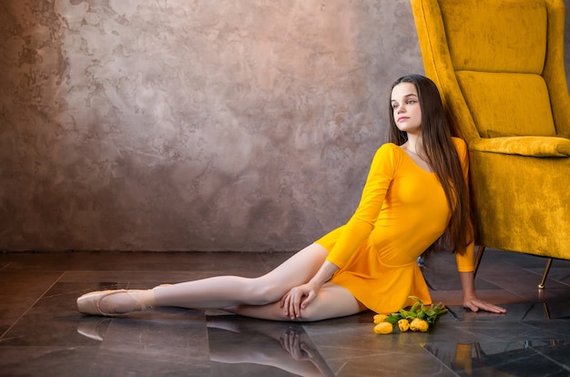 Una joven bailarina con un vestido amarillo y zapatos de punta se sienta con un ramo de tulipanes de primavera.
