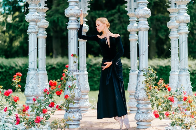 Joven bailarina en vestido antiguo negro posando en el arco en la naturaleza.