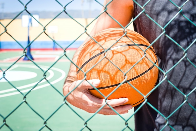 Joven con el baloncesto detrás de una valla de cerca