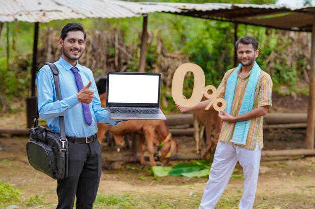 Joven banquero indio o agrónomo mostrando la pantalla del portátil con el agricultor en su granja
