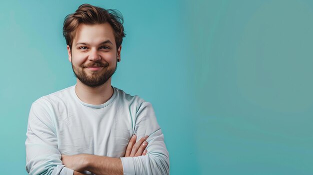 Foto un joven con barba y cabello castaño con una camisa blanca sonríe a la cámara con los brazos cruzados