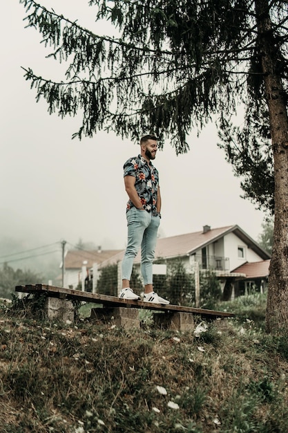 Joven con barba y camisa floreada posando en la naturaleza