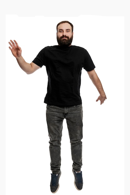 Un joven con barba está saltando. Preciosa morena con una camiseta negra y jeans grises. Altura completa. Aislado sobre fondo blanco. Vertical.