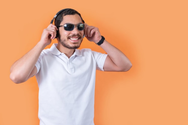Joven con barba y gafas de sol escuchando música con auriculares inalámbricos