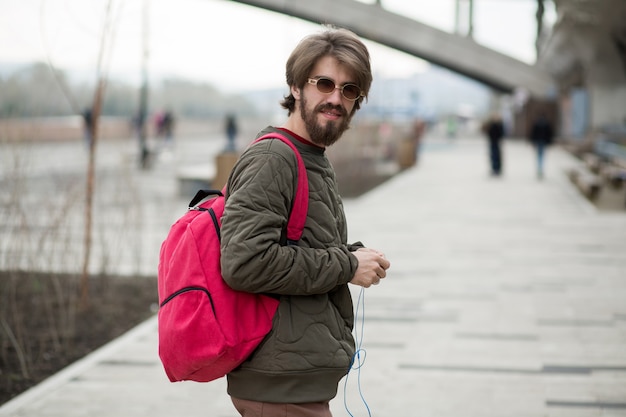 Joven con barba con una mochila y auriculares en la calle