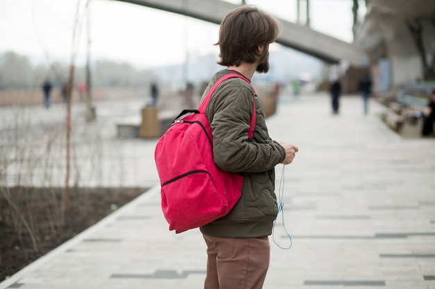 Joven con barba con una mochila y auriculares en la calle