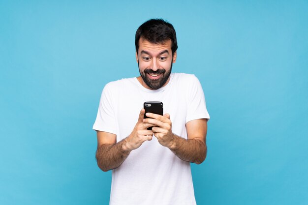 Joven con barba sobre pared azul aislado sorprendido y enviando un mensaje