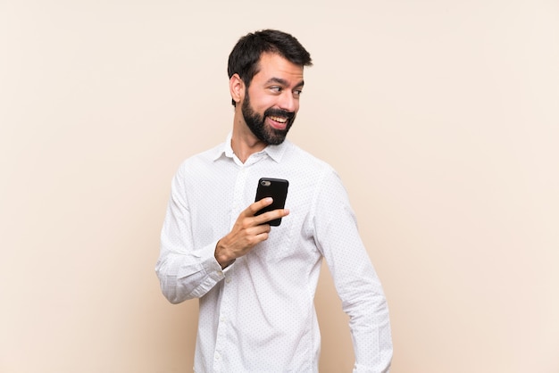 Joven con barba sosteniendo un móvil con los brazos cruzados y feliz