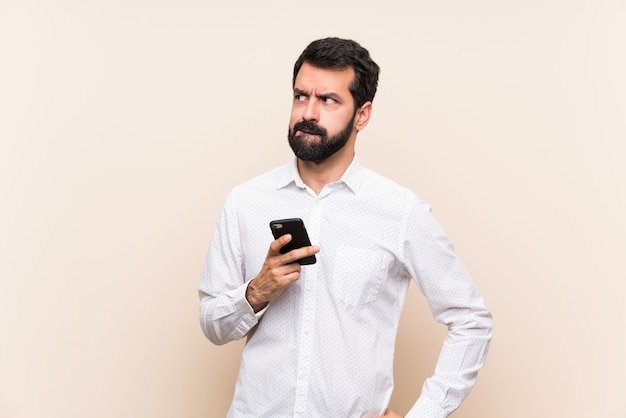 Joven con barba sosteniendo un móvil con expresión de la cara confusa