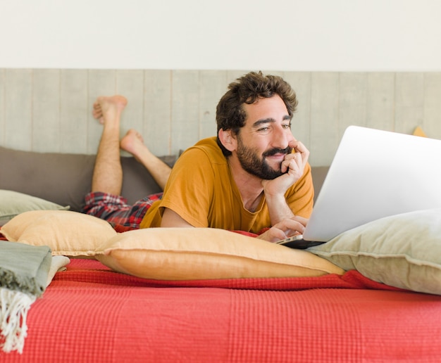 Joven barbudo en una cama con un portátil