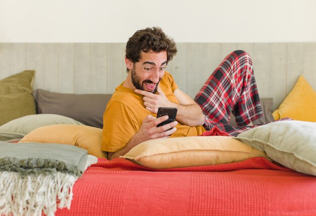 Joven barbudo en una cama con su teléfono móvil