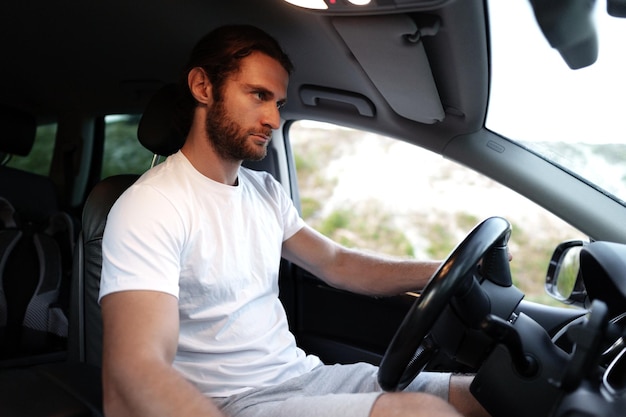 Un joven barbudo con una camiseta casual conduce un coche