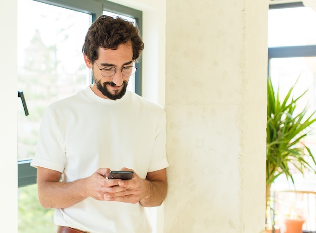 Joven barbudo en casa. usando un teléfono inteligente