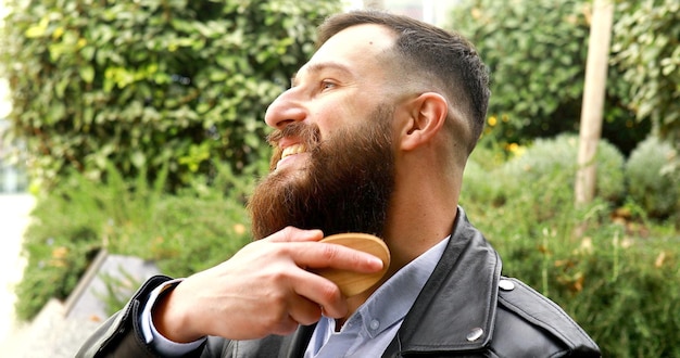 Joven barbudo cepillándose la barba al aire libre.