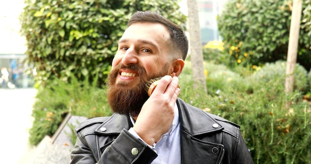 Joven barbudo cepillándose la barba al aire libre.