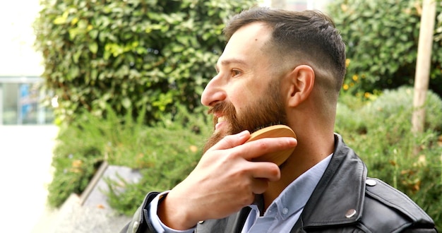 Joven barbudo cepillándose la barba al aire libre.