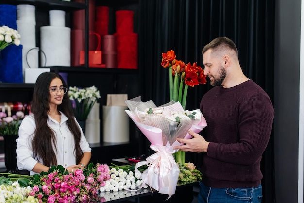 Un joven barbudo compra un hermoso ramo de flores para las vacaciones de una niña en una acogedora florería Floristería y fabricación de ramos en una floristería Pequeña empresa