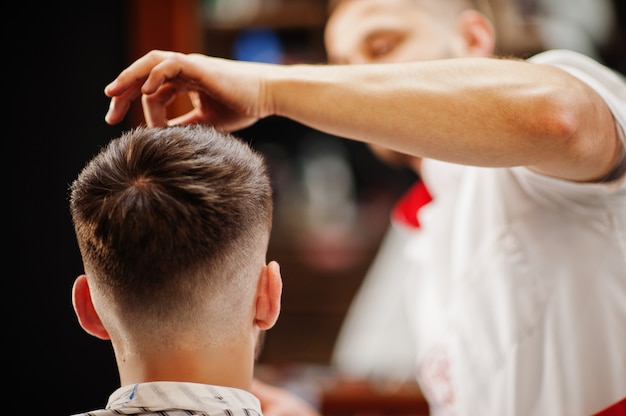 Joven barbudo corte de pelo por peluquero mientras está sentado en la silla en la barbería. alma de barbero.