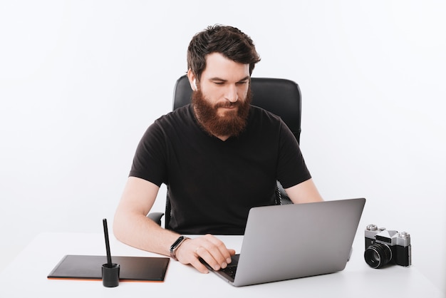 Joven barbudo está mirando la computadora en su escritorio.