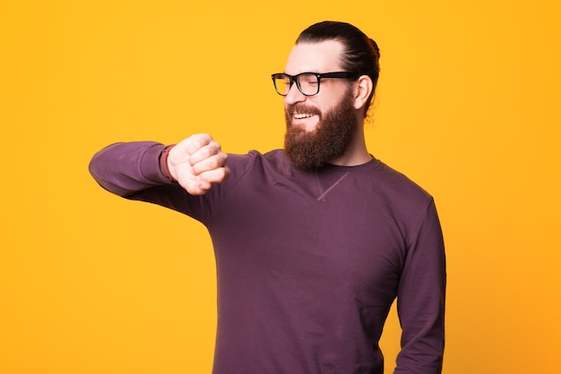 joven barbudo con gafas está sonriendo y mirando su reloj